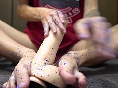 Young Girl Plays with Glitters and Gives Footjob to Big Dildo in Close Up